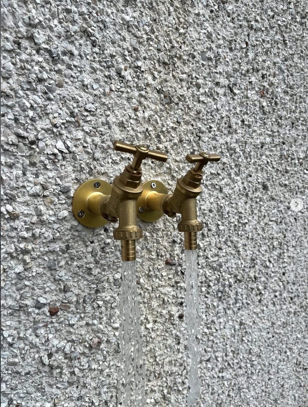 Two brass outside garden taps running against a pebbledash wall